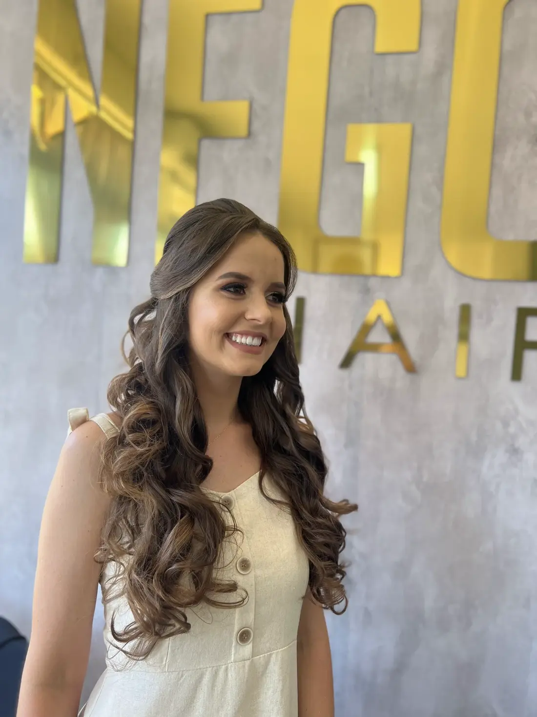 Penteado com cachos e mechas, painel dourado Nego Hair ao fundo