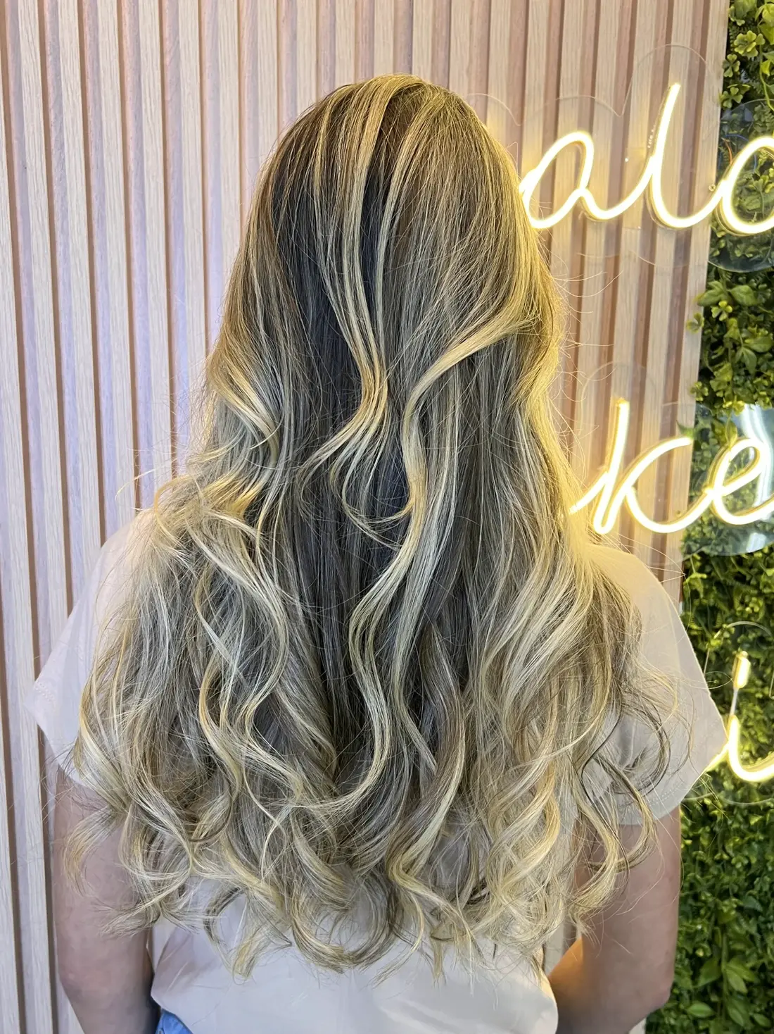 Cabelo loiro com mechas, letreiro do salão ao fundo
