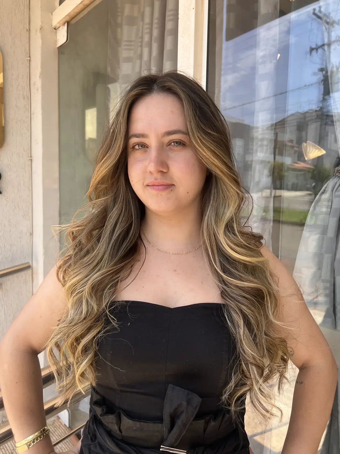 Cliente com mechas loiras em frente à vitrine do salão